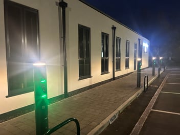 The Ratio io7 black charging pillar illuminated in ambient green light in front of a building.